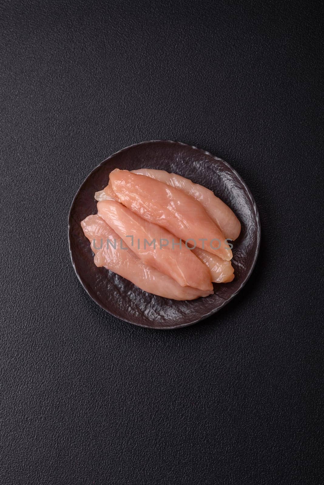 Raw chicken fillet cut into strips with spices and herbs on a wooden cutting board