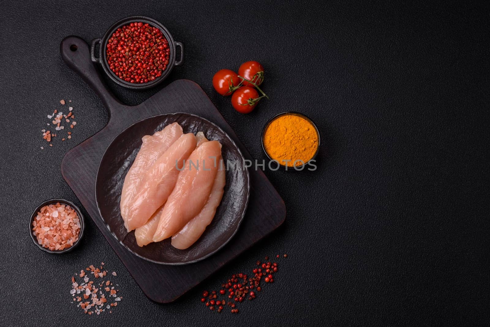 Raw chicken fillet cut into strips with spices and herbs on a wooden cutting board