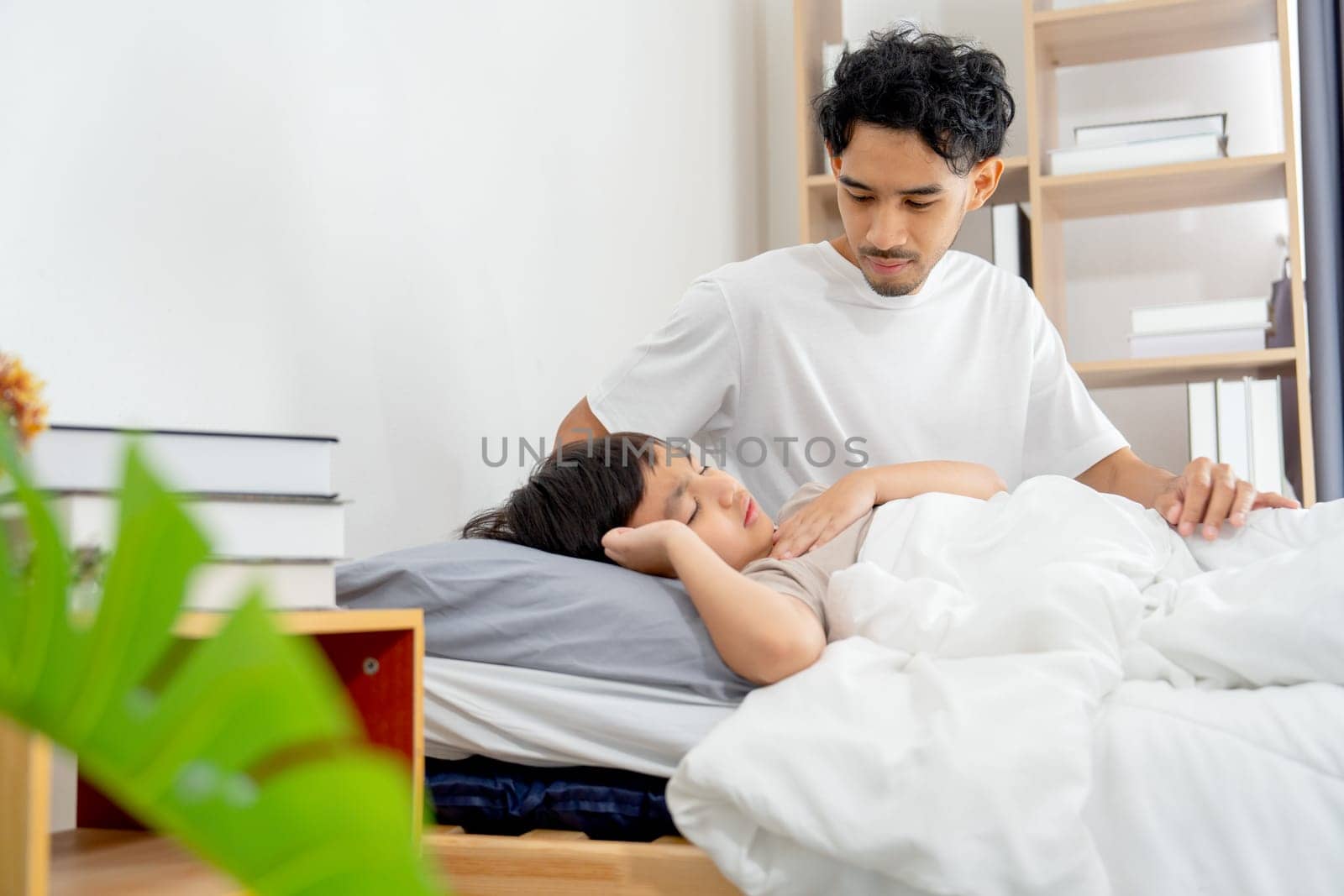 Asian young father sit near his son lie on bed with sick or unwell and father take care with love and support.