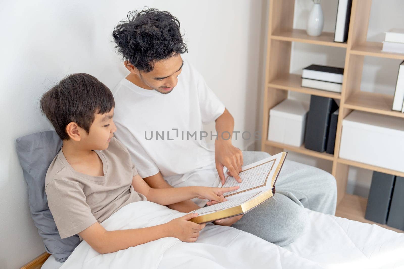 Top view Asian young father sit near his son on bed and read the book together with happiness and day light.
