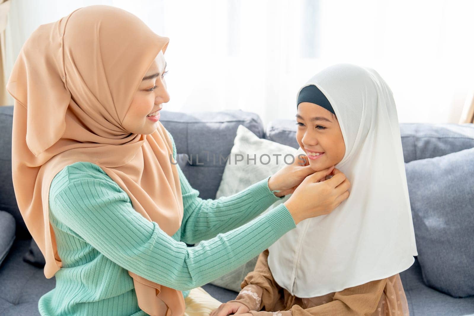 Close up Asian muslim mother help her daughter to wear headscarf or hijab for her and stay in living room of their house with day light and happiness.