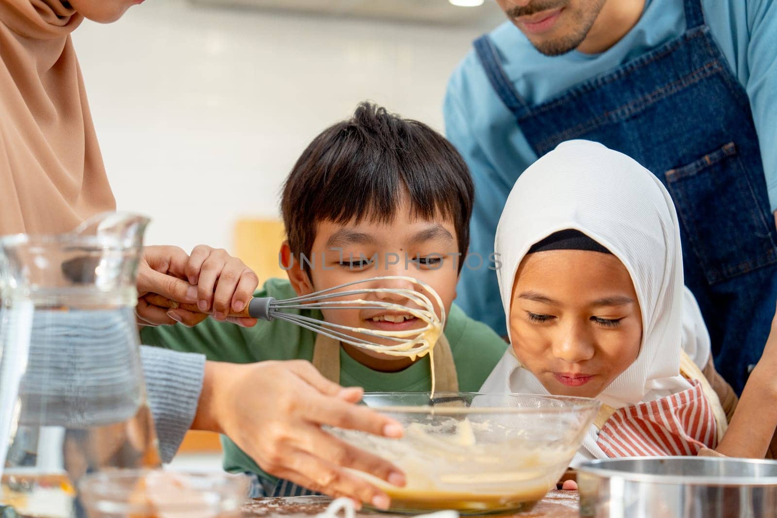 Little Asian boy and girl show smell action after mix flour in the bowl and enjoy with family in the kitchen of their house.