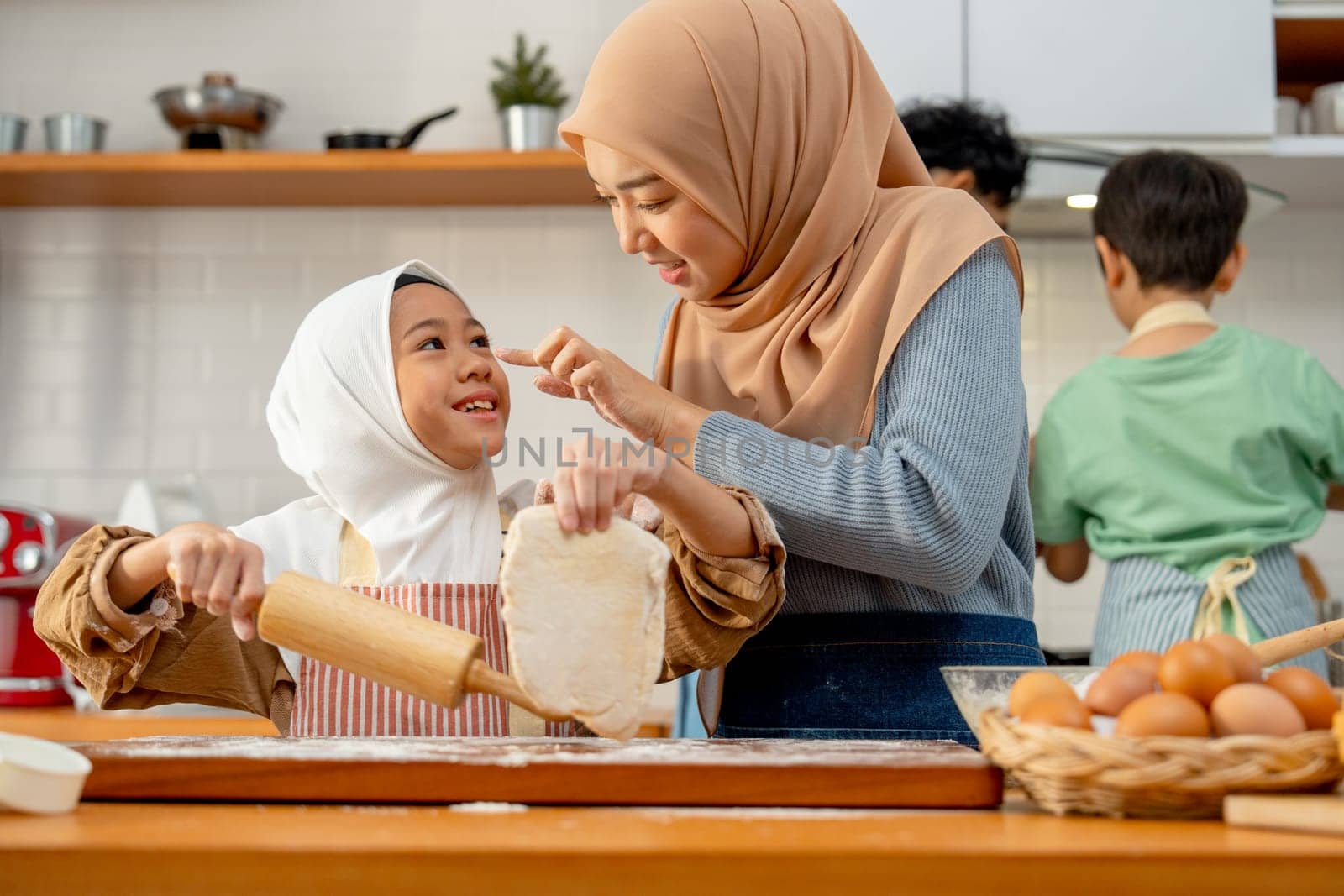 Young Asian muslim mother and daughter tease and enjoy to make some bakery together in the kitchen.