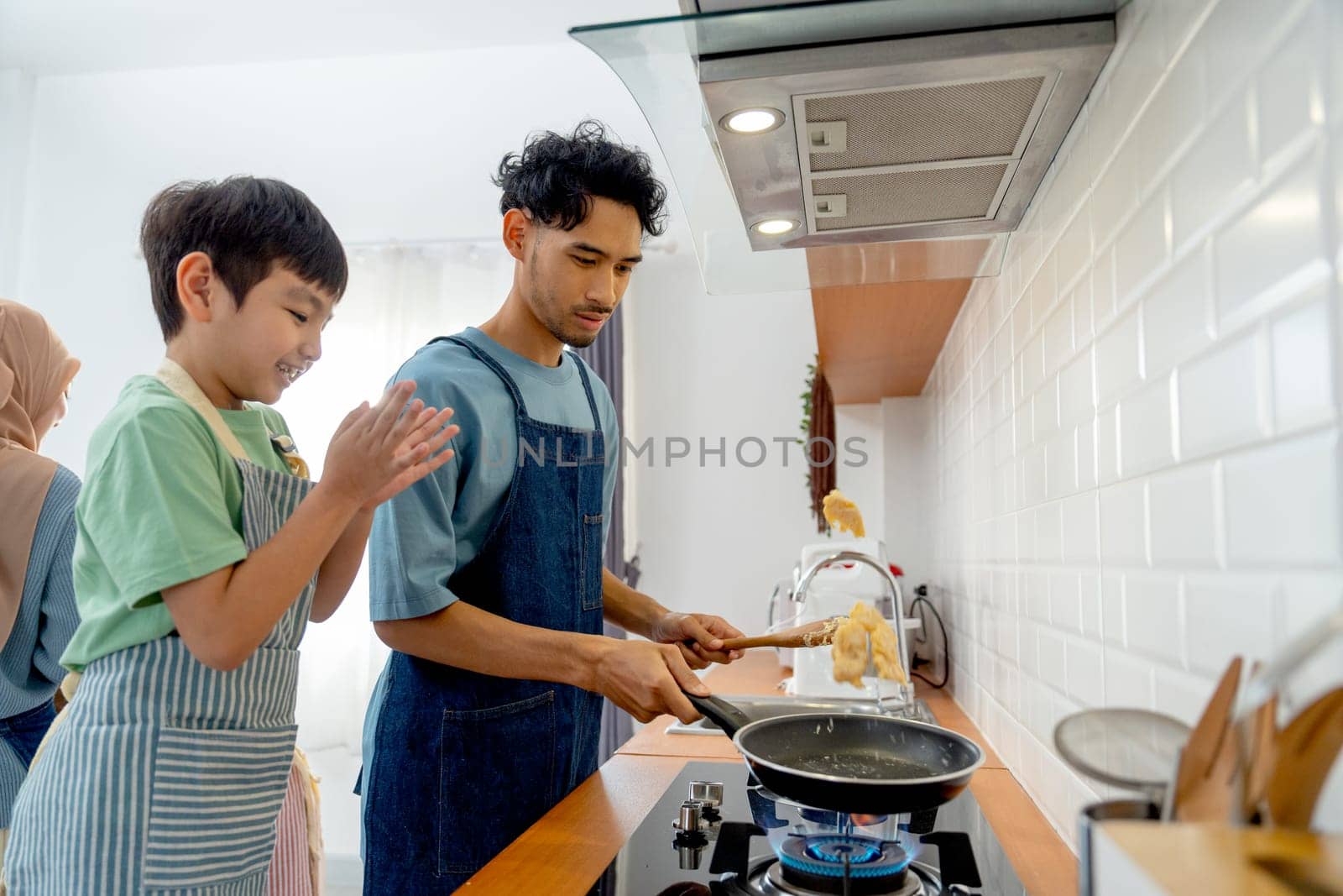 Side view young Asian father show skill of cooking by throwing pan cake up and his son cheer up beside in the kitchen of their house.