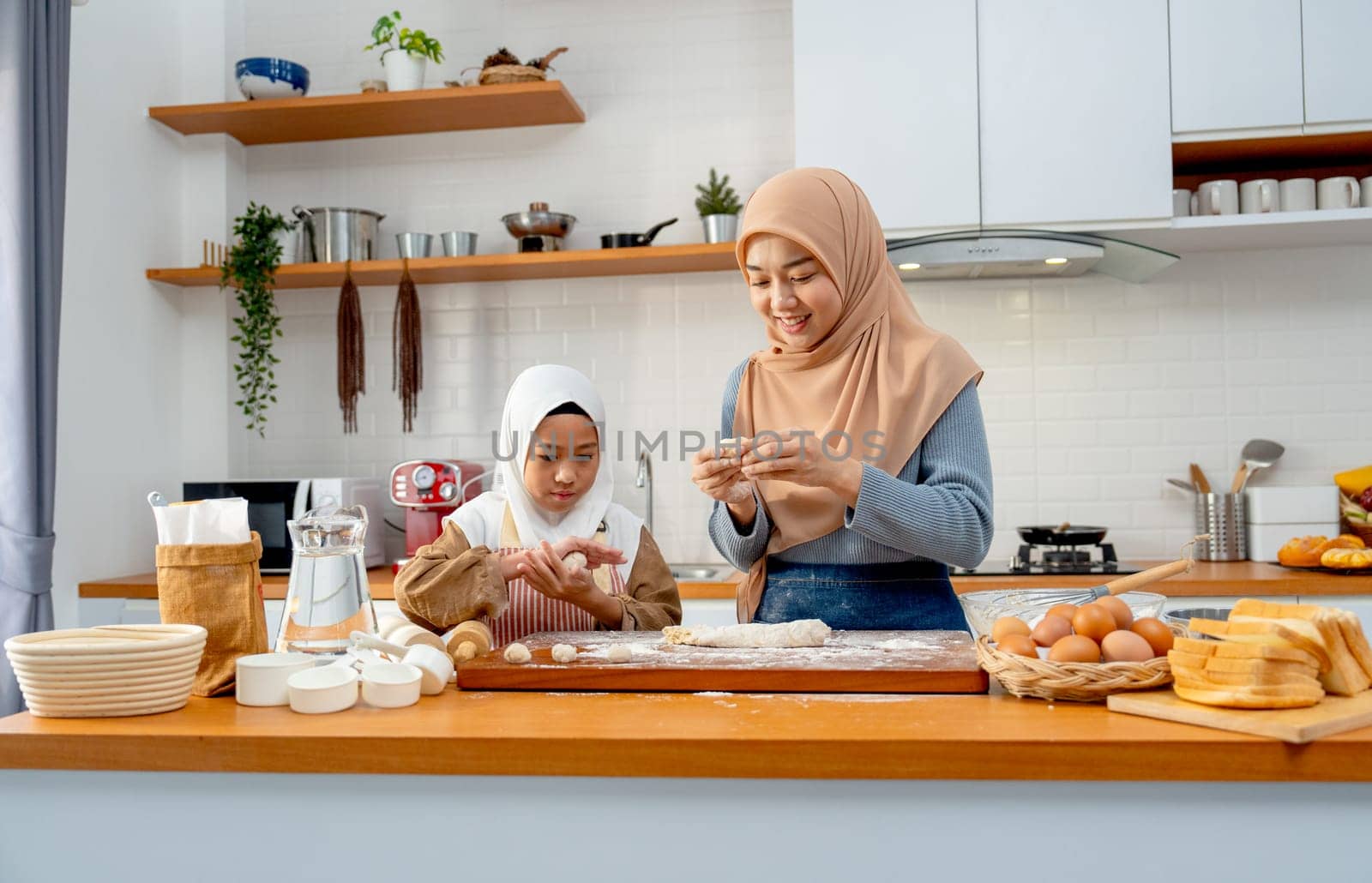 Wide shot of Asian muslim mother teach her daughter to threshing flour to be like ball shape for making bakery together in kitchen of their house.