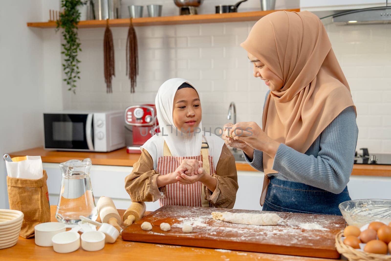 Side view of Asian muslim mother teach her daughter to threshing flour to be like ball shape for making bakery together in kitchen of their house.