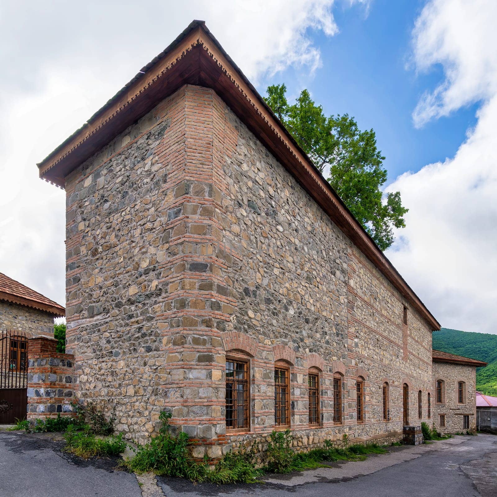Historic stone building in Shaki, Azerbaijan features traditional architecture with stone wall, large windows and a rustic facade