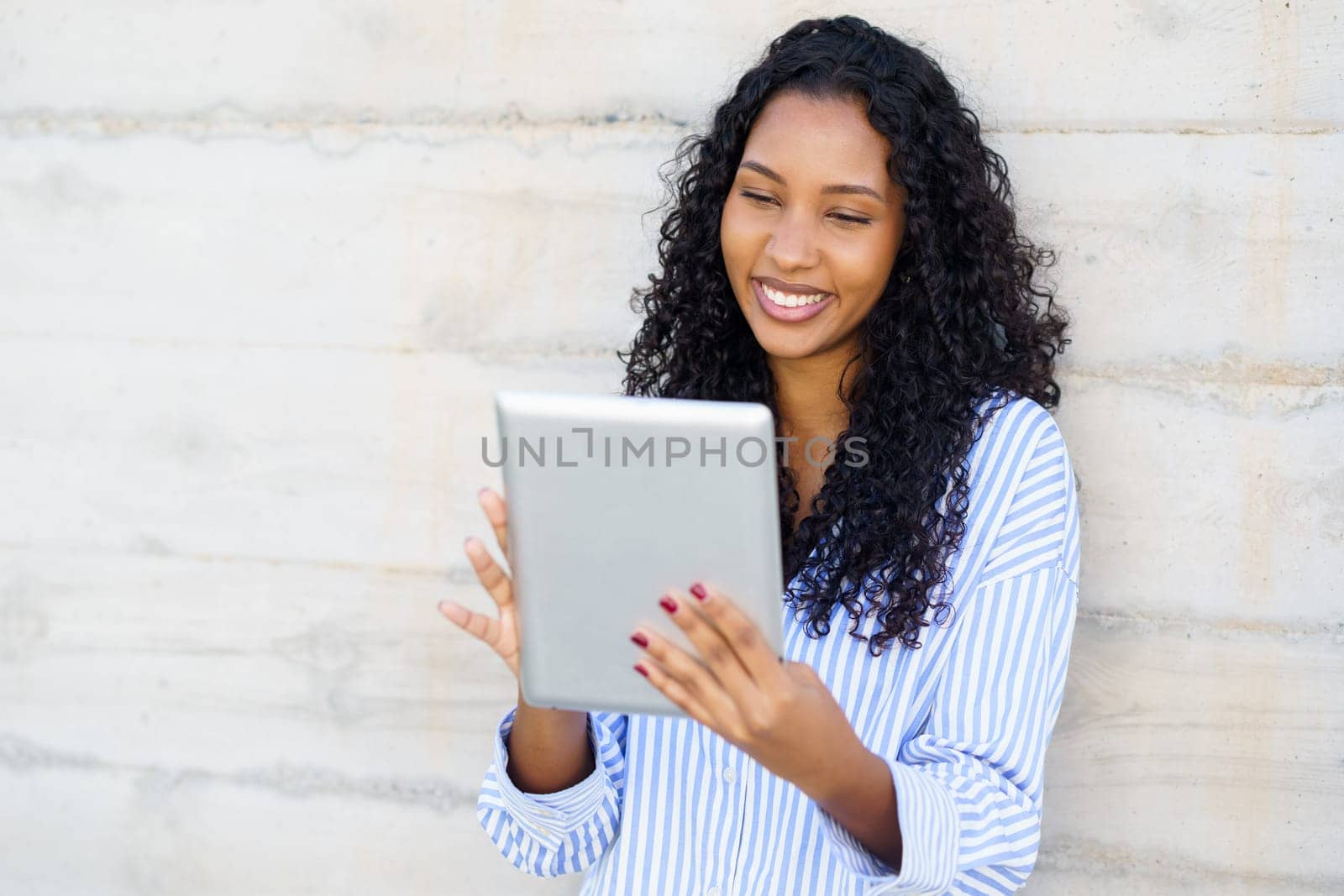 A cheerful and vibrant young woman actively enjoys using her tablet outdoors, showcasing her engagement with the modern world of technology. Ideal for themes focusing on lifestyle and tech innovation