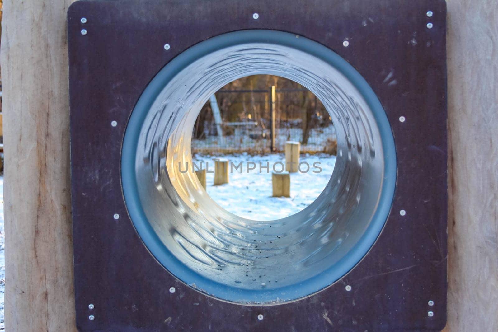 Children can enjoy outdoor playtime in a snowy park featuring a large slide opening, surrounded by wooden posts and trees.