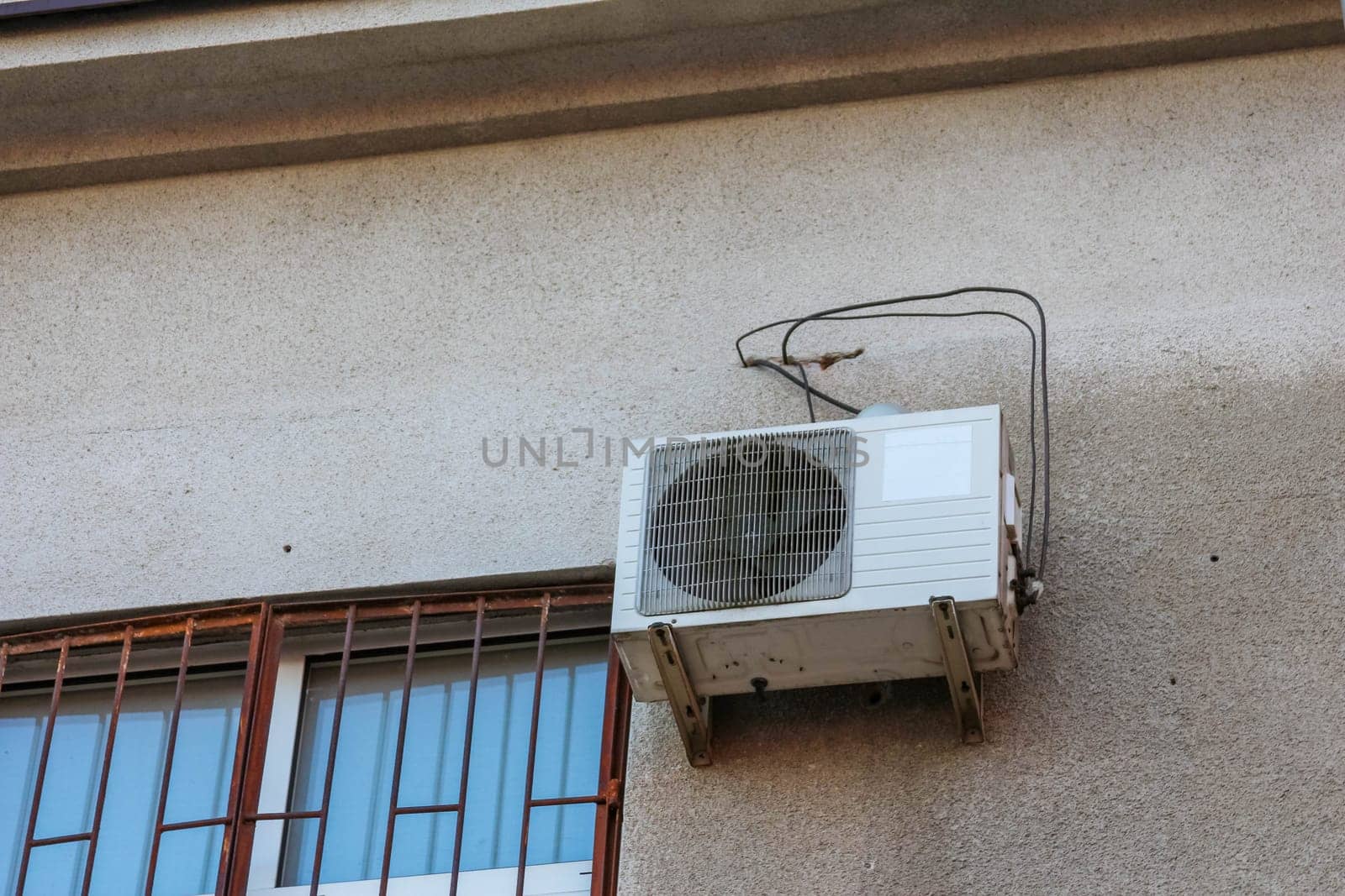An exterior air conditioning unit is mounted on a building wall, providing cooling during the hot summer months. The sun casts a warm glow.