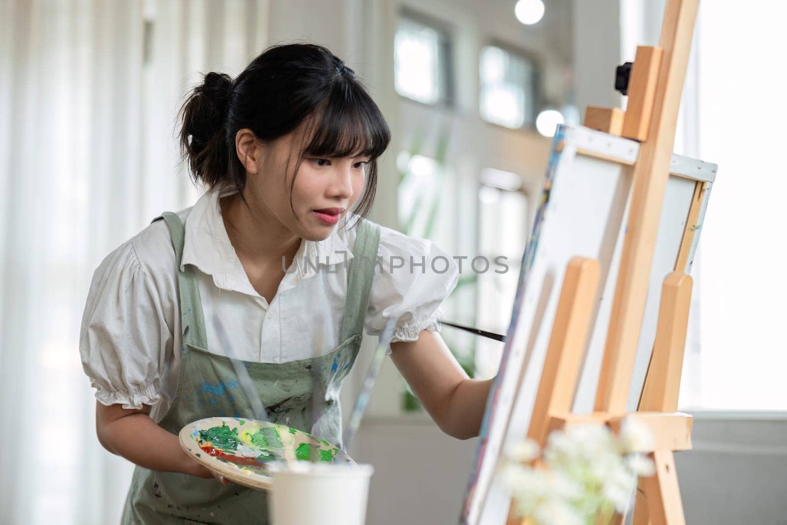 Young female artist works on abstract acrylic painting on canvas in art painting studio..