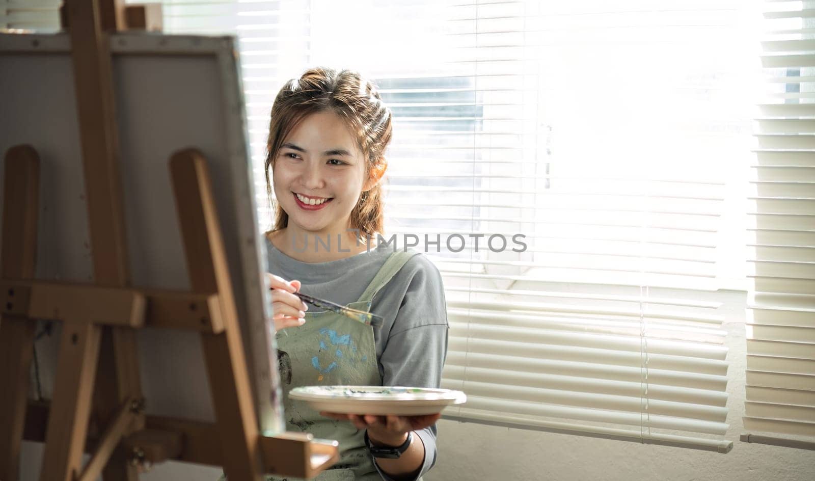 Young female artist works on abstract acrylic painting on canvas in art painting studio..