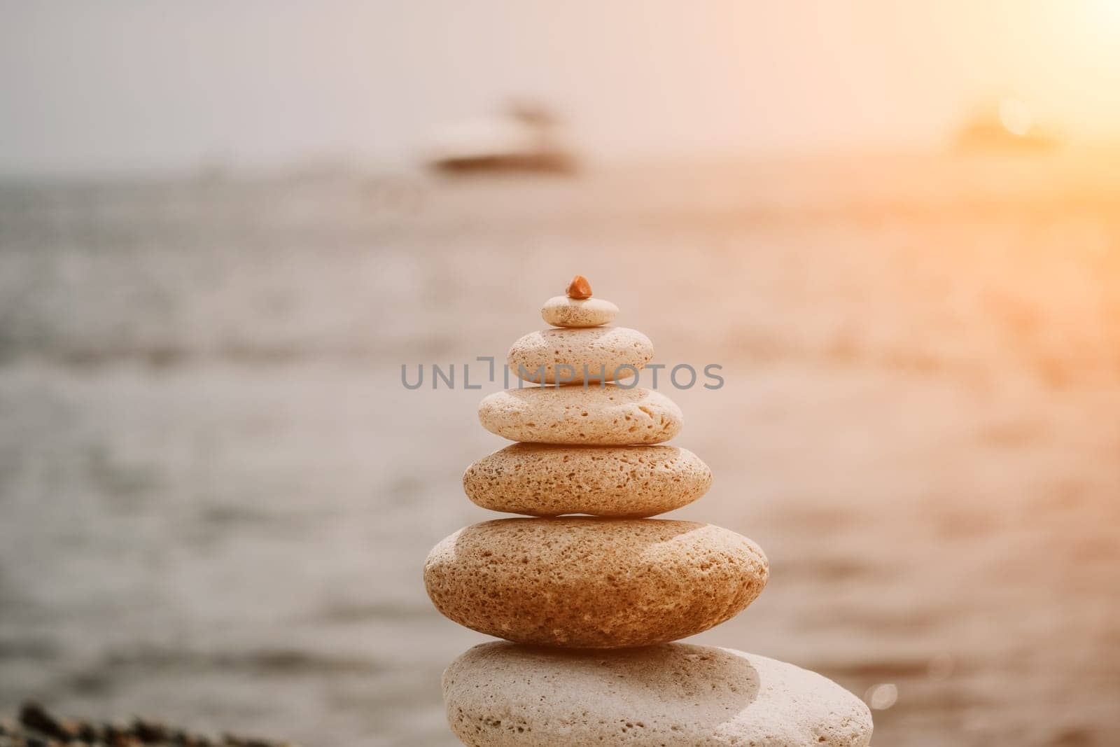 Pyramid stones on the seashore with warm sunset on the sea background. Happy holidays. Pebble beach, calm sea, travel destination. Concept of happy vacation on the sea, meditation, spa, calmness.