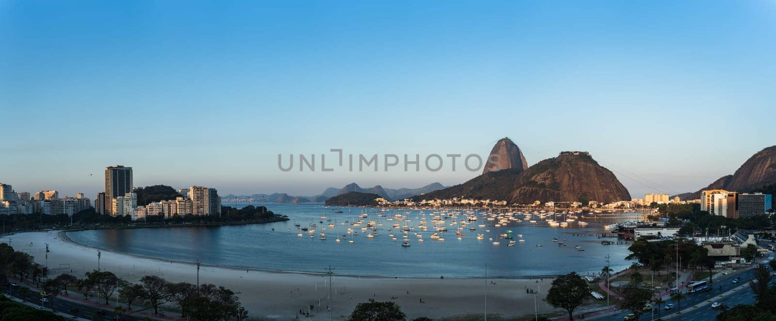 Beautiful dusk view of Botafogo, Rio de Janeiro, with highlights like Sugarloaf Mountain, Urca Hill, sailboat-filled bay and an empty beach. Ideal for text placement.