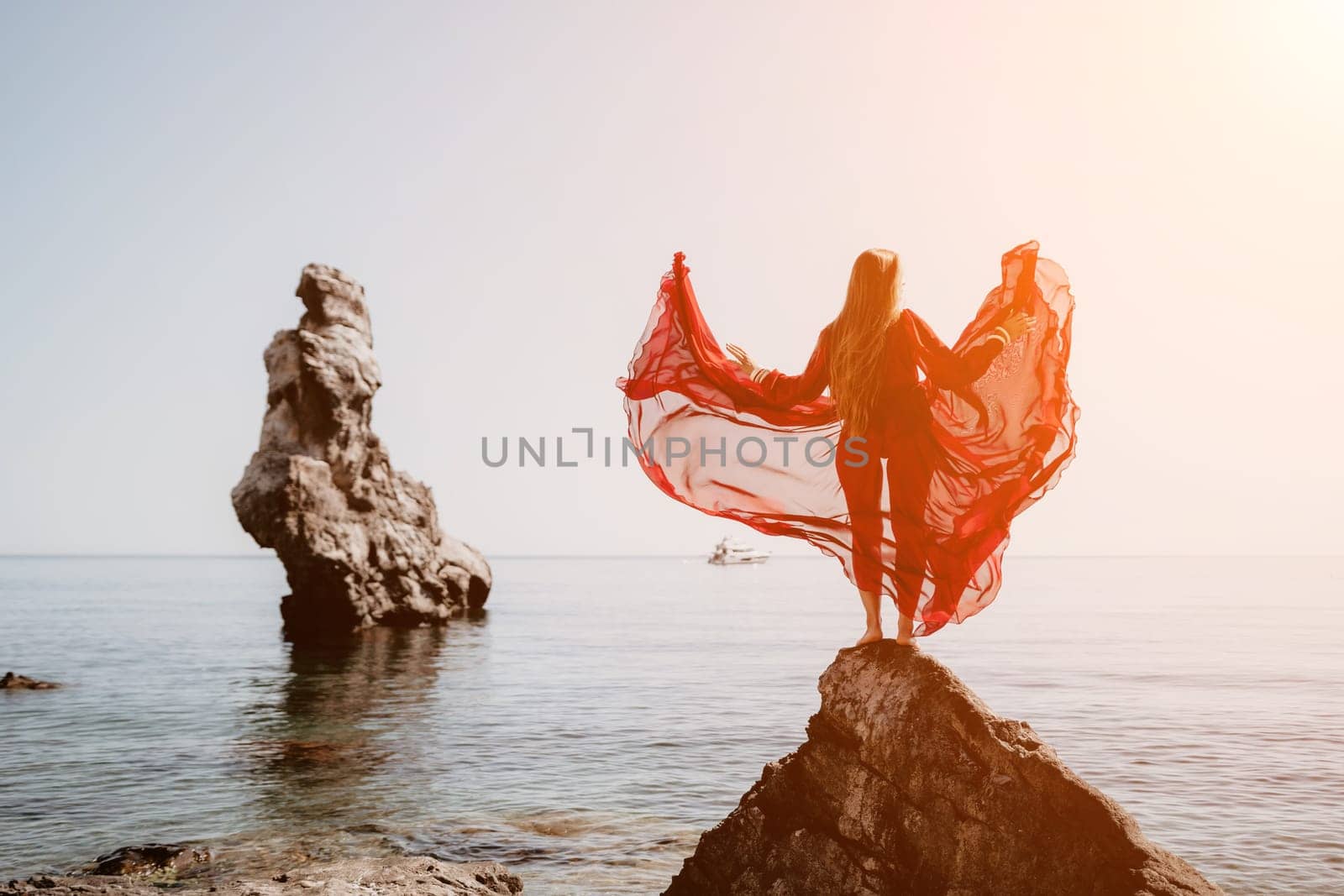 Woman travel sea. Young Happy woman in a long red dress posing on a beach near the sea on background of volcanic rocks, like in Iceland, sharing travel adventure journey by panophotograph