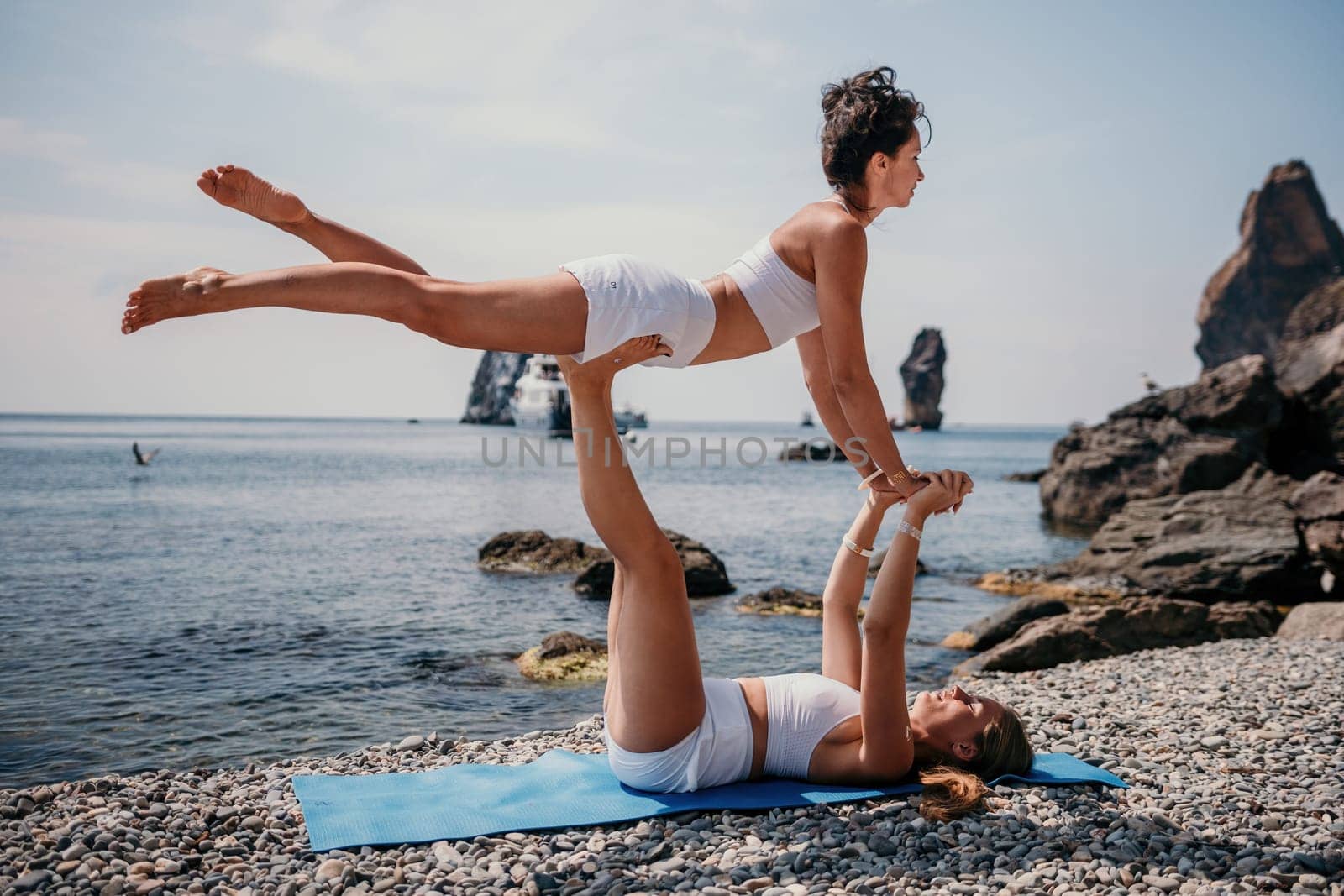 Woman sea yoga. Two Happy women meditating in yoga pose on the beach, ocean and rock mountains. Motivation and inspirational fit and exercising. Healthy lifestyle outdoors in nature, fitness concept. by panophotograph