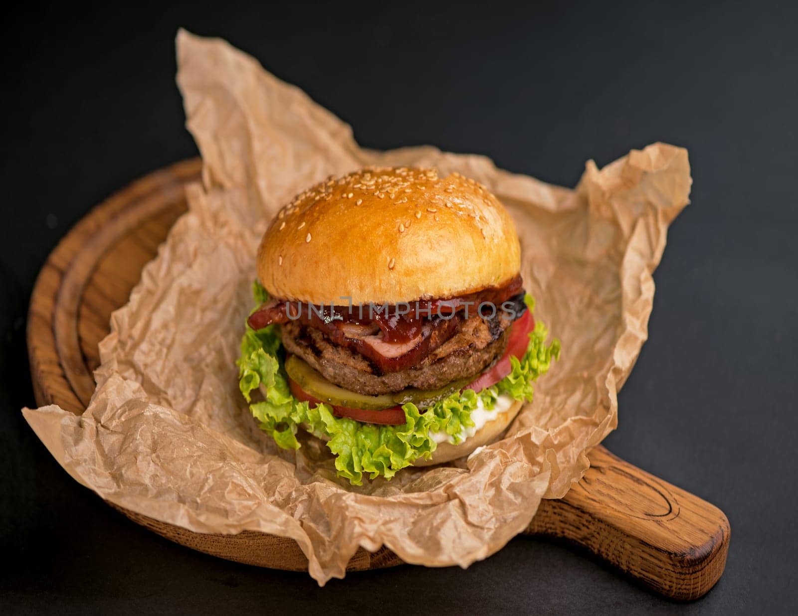 Big tasty burger with beef patty, lettuce, bacon and pickle on black background by aprilphoto