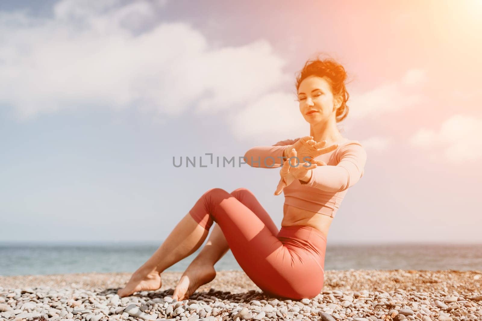 Middle aged well looking woman with black hair, fitness instructor in leggings and tops doing stretching and pilates on yoga mat near the sea. Female fitness yoga routine concept. Healthy lifestyle by panophotograph