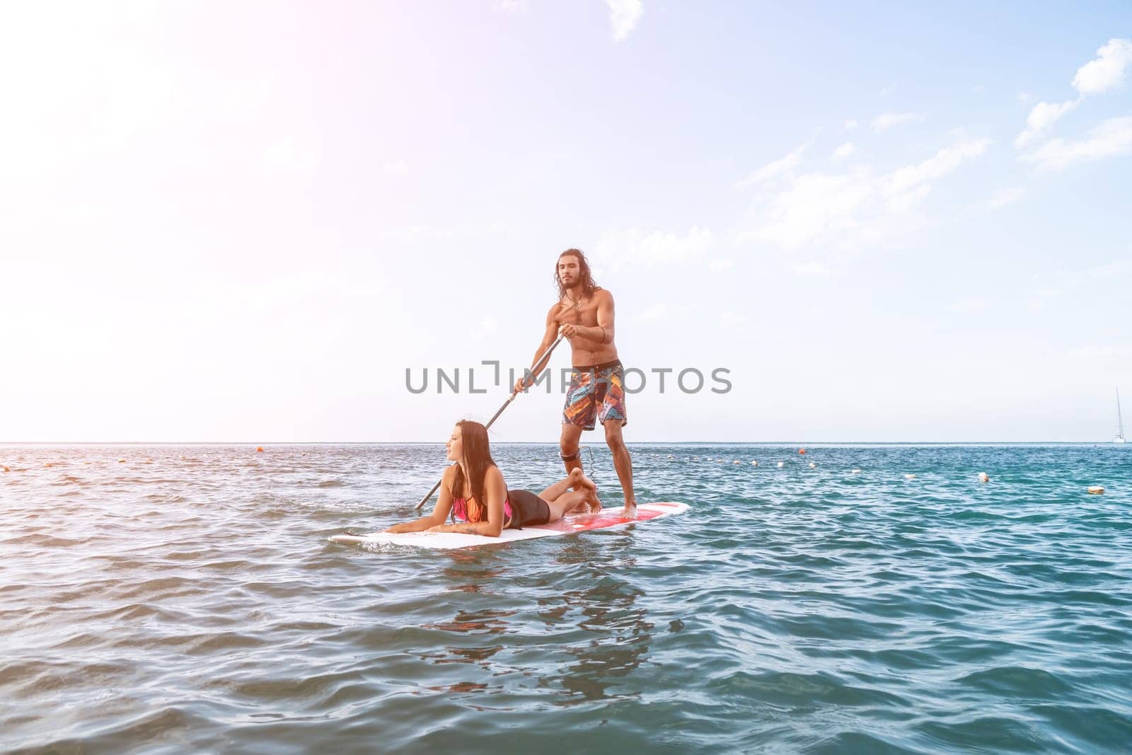 Sea woman and man on sup. Silhouette of happy young woman and man, surfing on SUP board, confident paddling through water surface. Idyllic sunset. Active lifestyle at sea or river. by panophotograph