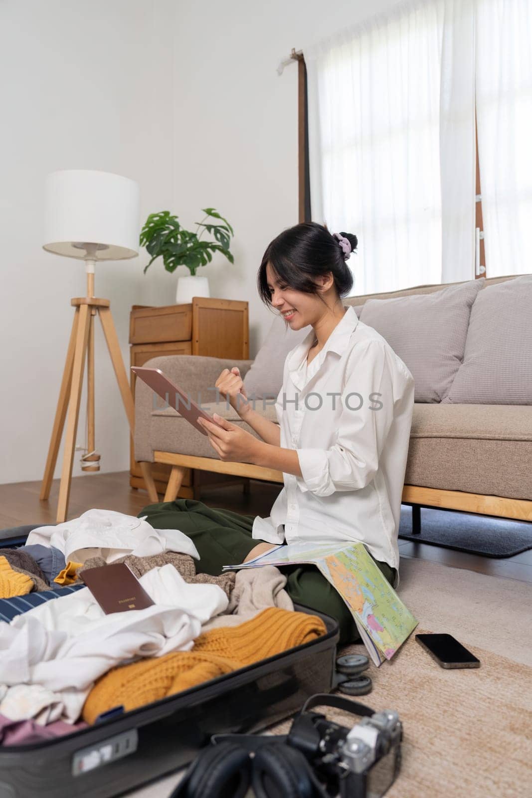 Asian woman while playing tablet success booking flight ticket and prepare to traveling trip on holiday. Young cute woman using tablet to searching for a trip on weekend at home by nateemee