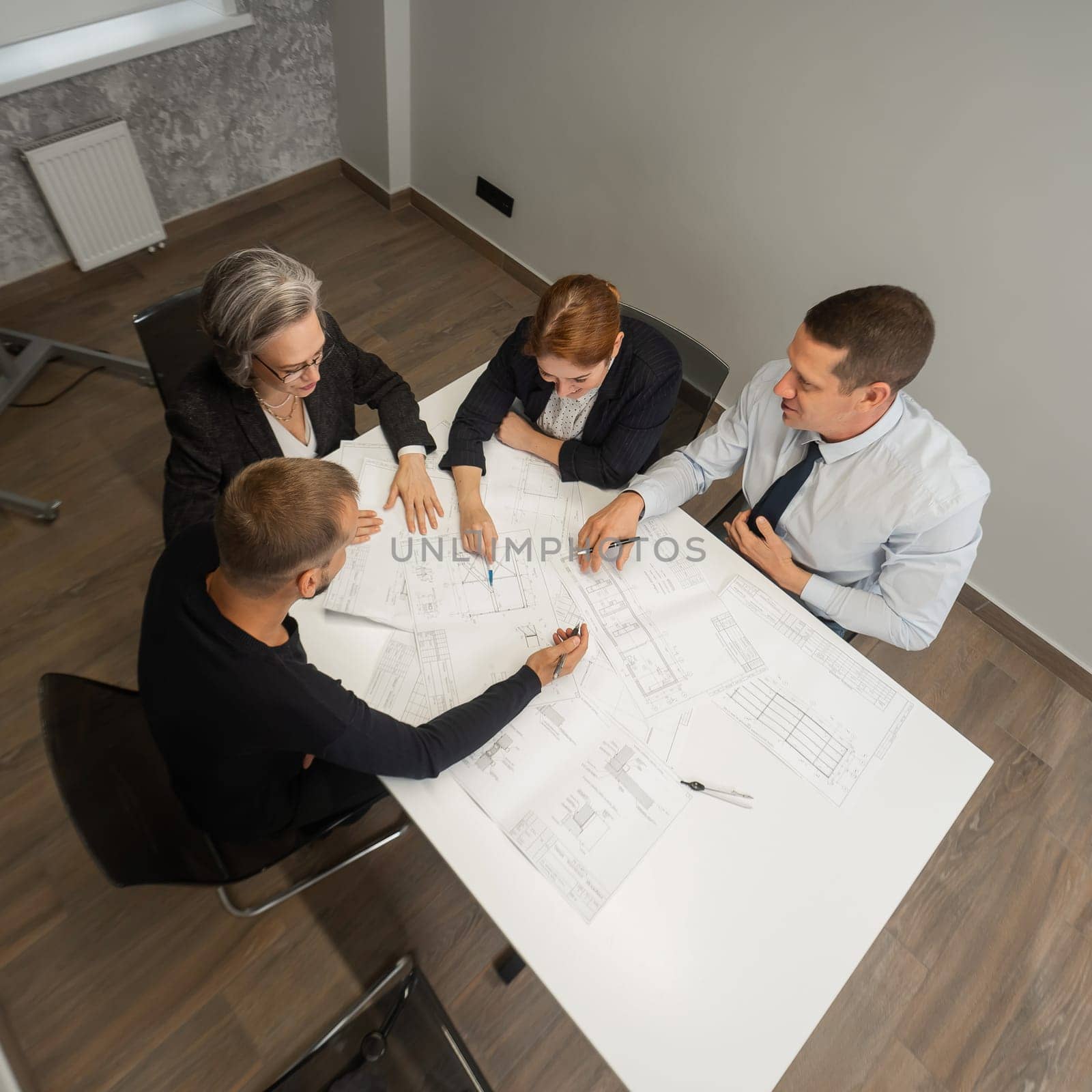 Top view of 4 business people sitting at a table and discussing blueprints. Designers engineers at a meeting