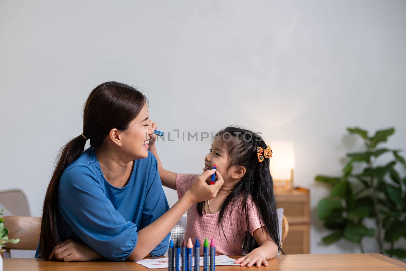 A young family spends their free time together in the living room at home. Mother and little daughter draw pictures with crayons on paper, smiling happy. by wichayada