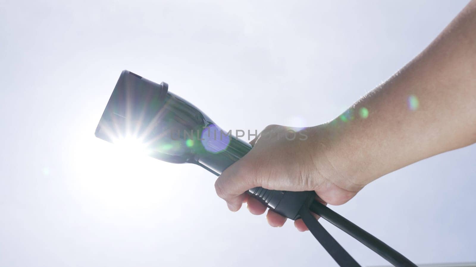 Closeup hand grasping an EV plug for electric vehicle with the midday sky in the background as progressive idea of alternative sustainable clean and green energy for environmental concern.