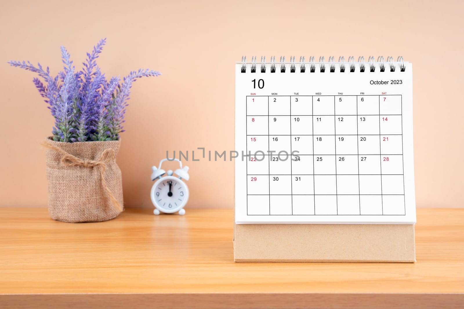 October Monthly desk calendar for 2023 year and alarm clock on wooden table.