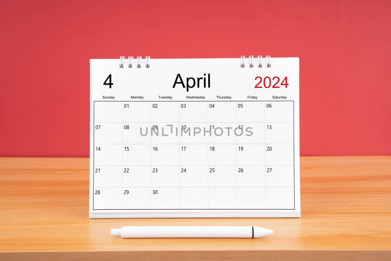 The April monthly desk calendar for 2024 year and pen on wooden table with red color background. by Gamjai