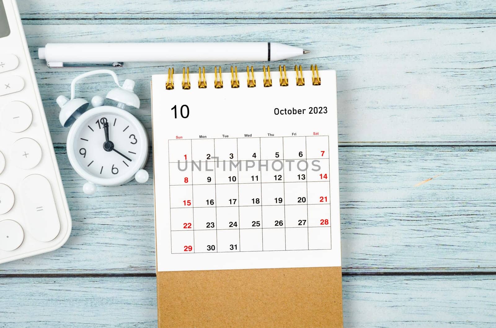 The October 2023 Monthly desk calendar for the organizer to plan 2023 year with alarm clock and pen on wooden table. by Gamjai