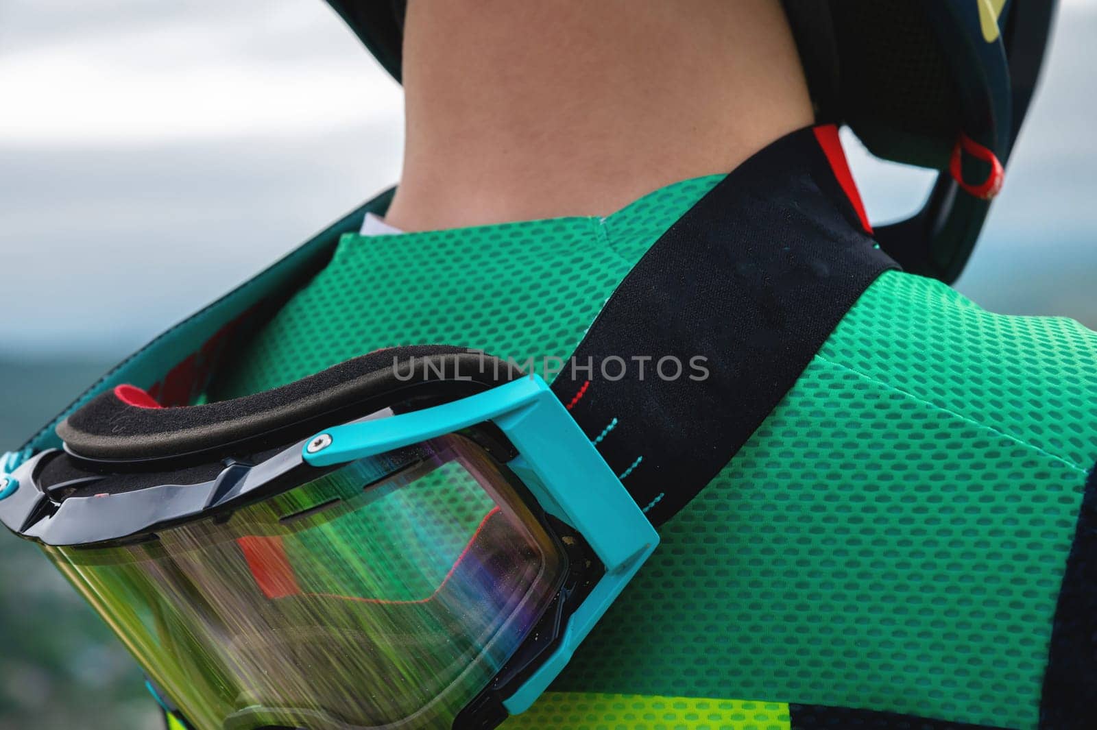 Close-up of protective goggles mask on the neck of a young cyclist rider outdoors. View from the back.