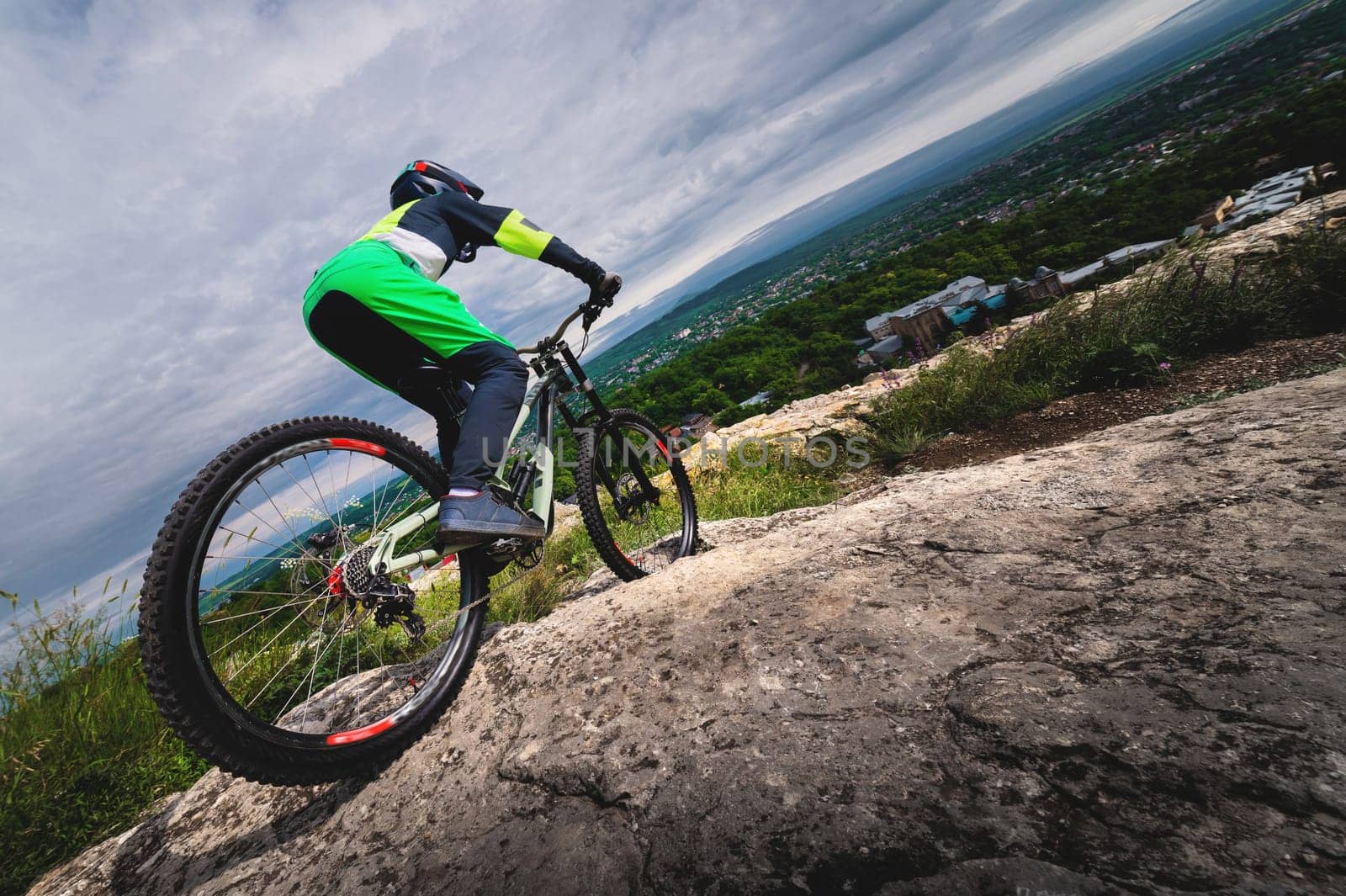 A young cyclist rides off a cliff on his mountain bike against the backdrop of the private sector of the village. Wide angle low angle with obstructed horizon by yanik88