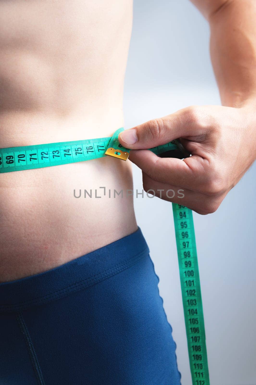 vertical photo of a man's hand measuring his waist with a centimeter after a workout on a white background. unrecognizable young man.