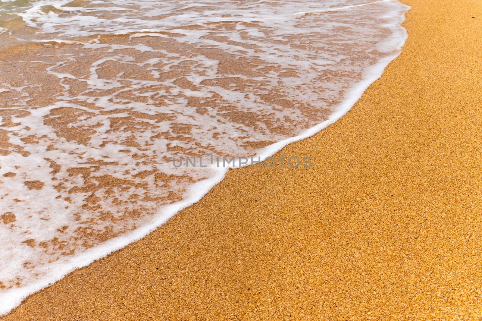 an ocean wave hits the sandy sand. Background with sea foam on golden sand beach, top view.