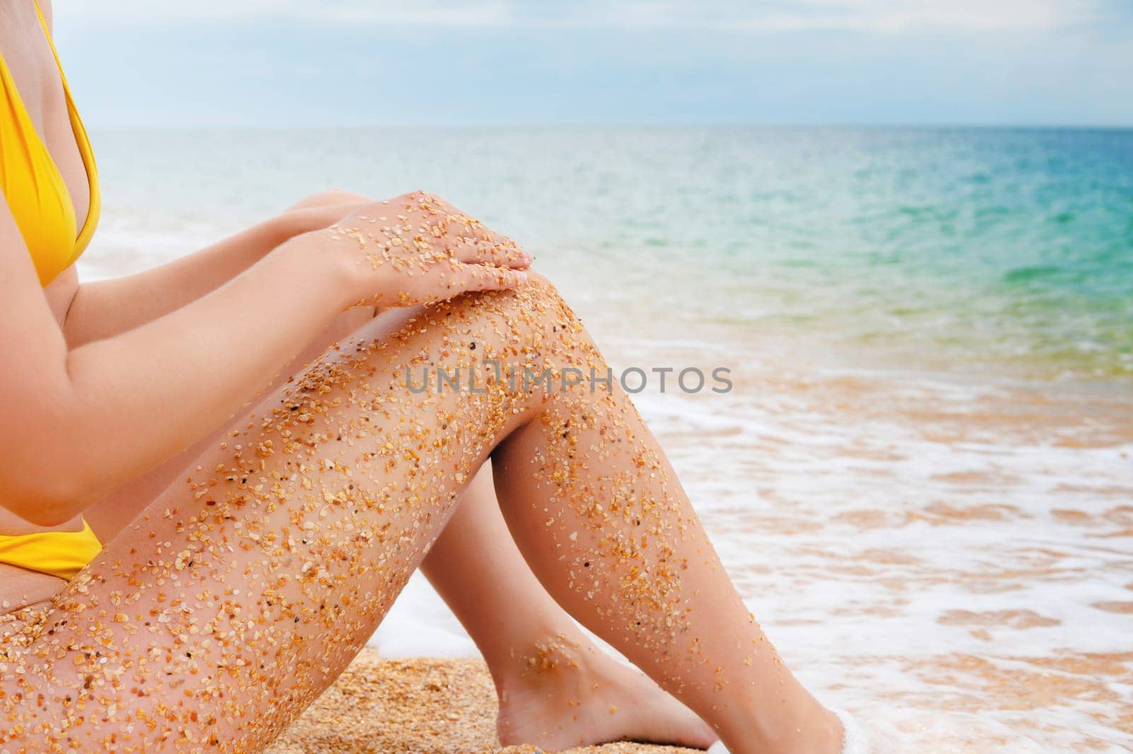 close-up shot of wet sand clinging to the feet of a girl sitting on the sea in a swimsuit, in daylight. Sandy feet of an unrecognizable woman on the beach by yanik88