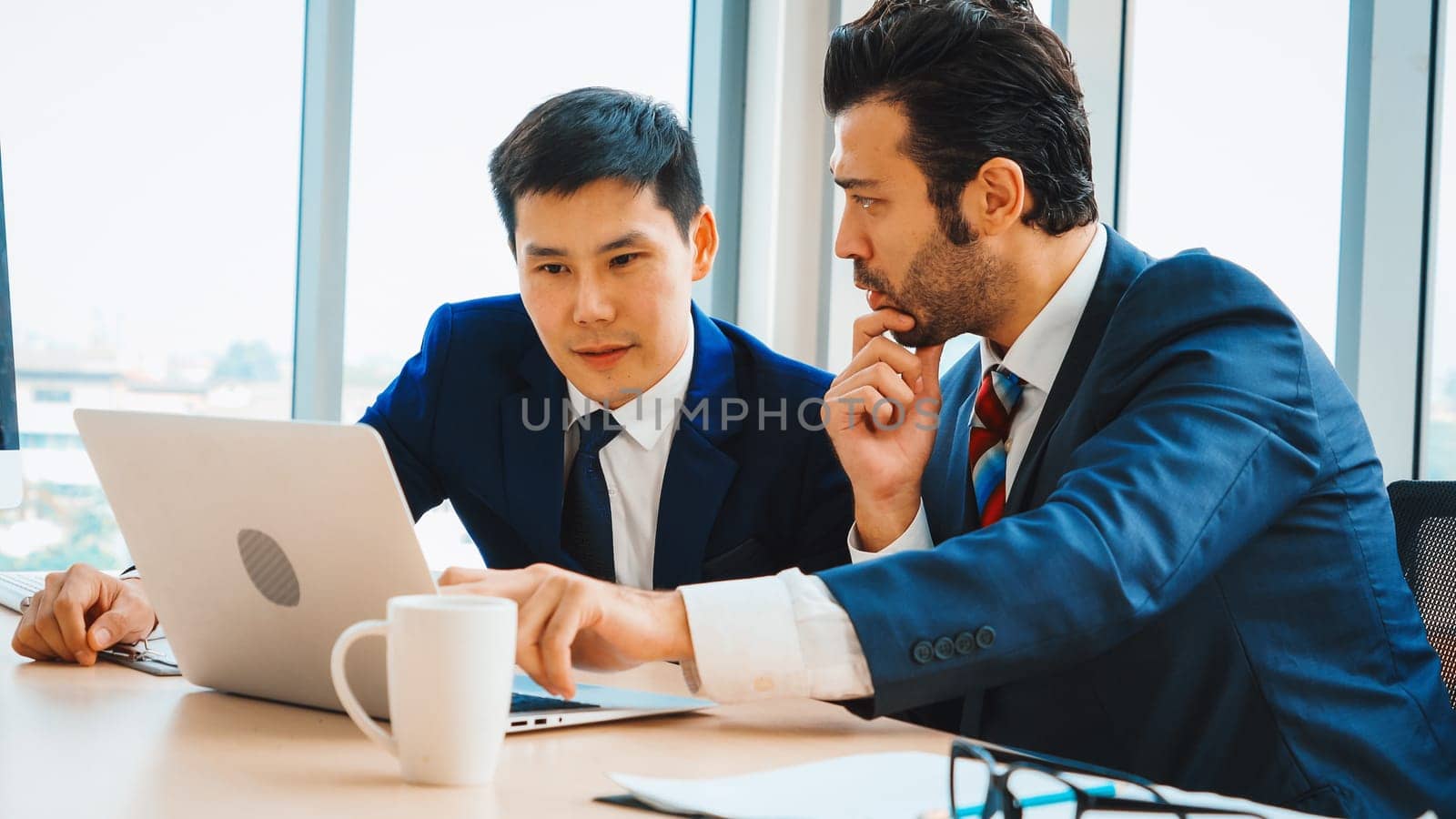 Two business people talk project strategy at office meeting room. Businessman discuss project planning with colleague at modern workplace while having conversation and advice on financial report. Jivy