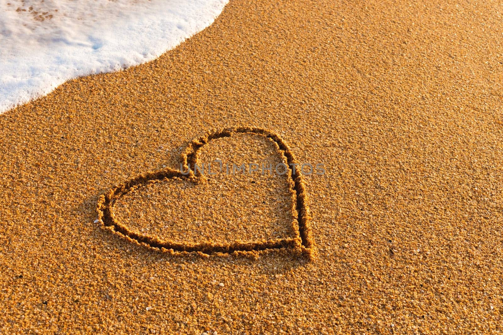 Heart drawn on the beach. hand written love sign on the sand with a wave in the background.