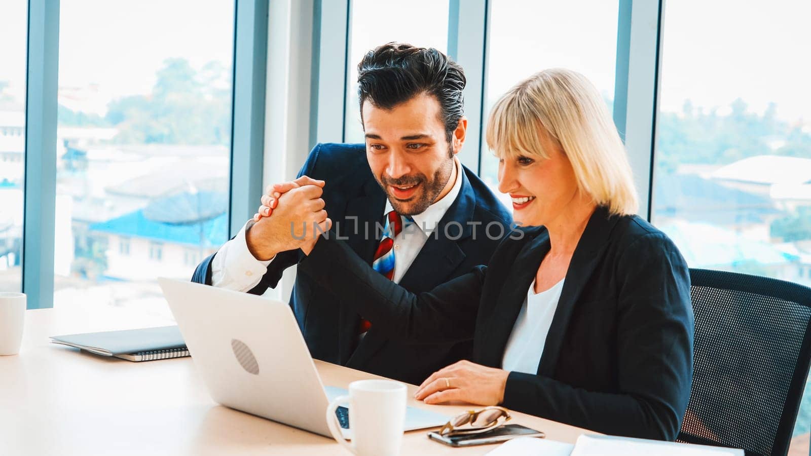 Two happy business people celebrate at office meeting room. Successful businessman congratulate project success with colleague at modern workplace while having conversation on financial report. Jivy