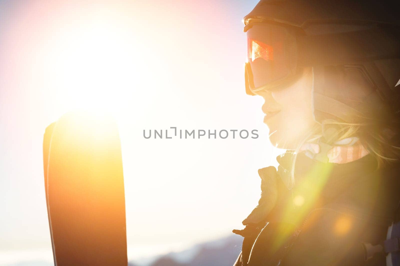 Ski portrait of a woman in a helmet, cool ski goggles on a cold sunny day. A smiling girl in profile stands in the mountains and looks at the beautiful views.