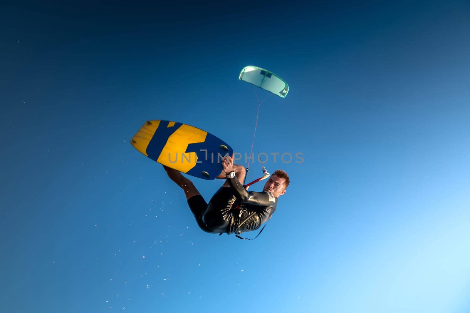professional kiter performs a difficult trick against a beautiful blue sky background. Kitesurfing, Caucasian young man jump among clear sky by yanik88