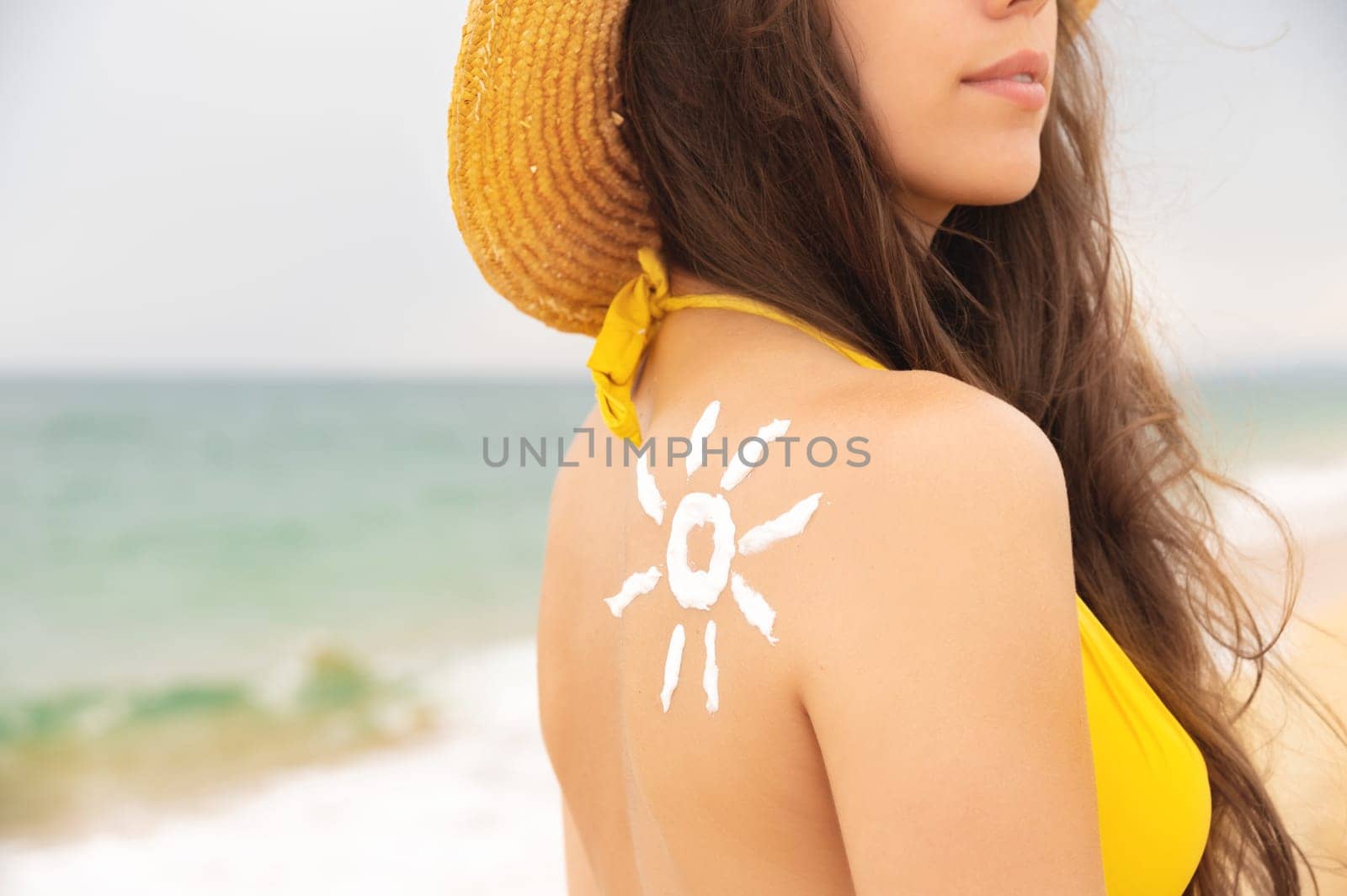 Attractive young Caucasian woman in a yellow swimsuit with sunblock on her shoulder in the form of the sun. Sea summer sun healthy skin.