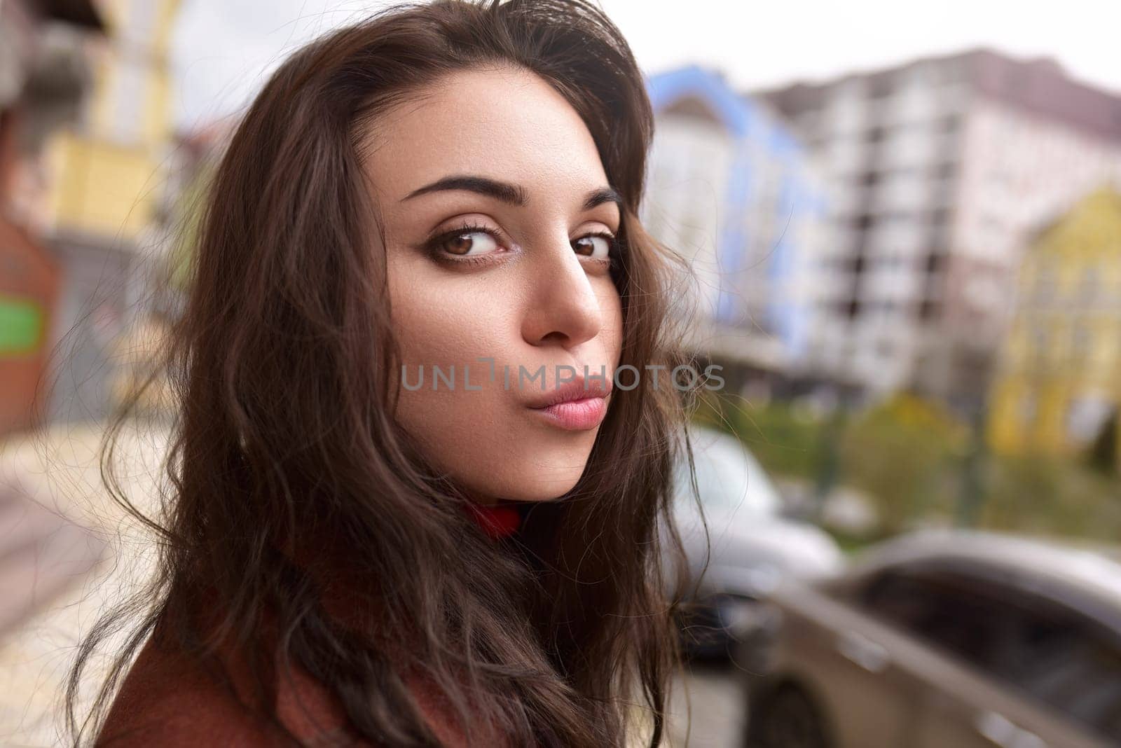 A beautiful fashionable lady in an autumn brown coat sends a kiss on the street.