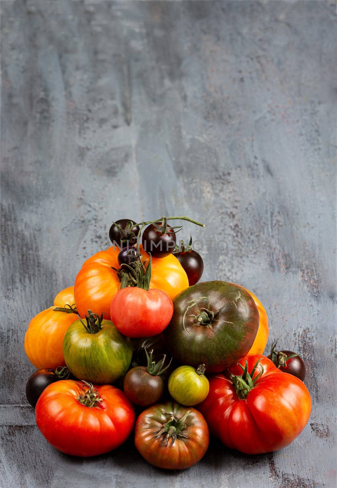 pile of freshly old tomatoes harvested heirloom and heritage tomatoes from the garden Multicoloured, red, green, black, purple, orange and yellow tomatoes on grey background by JPC-PROD