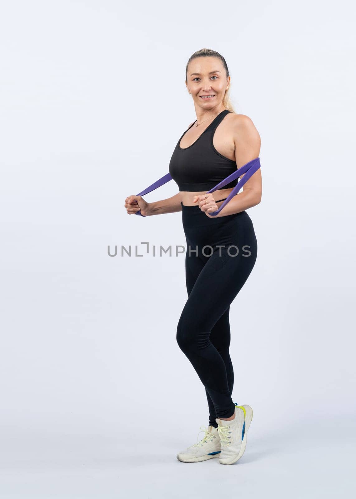 Full body length shot athletic and sporty senior woman with fitness resistance band on isolated background. Healthy active physique and body care lifestyle after retirement. Clout