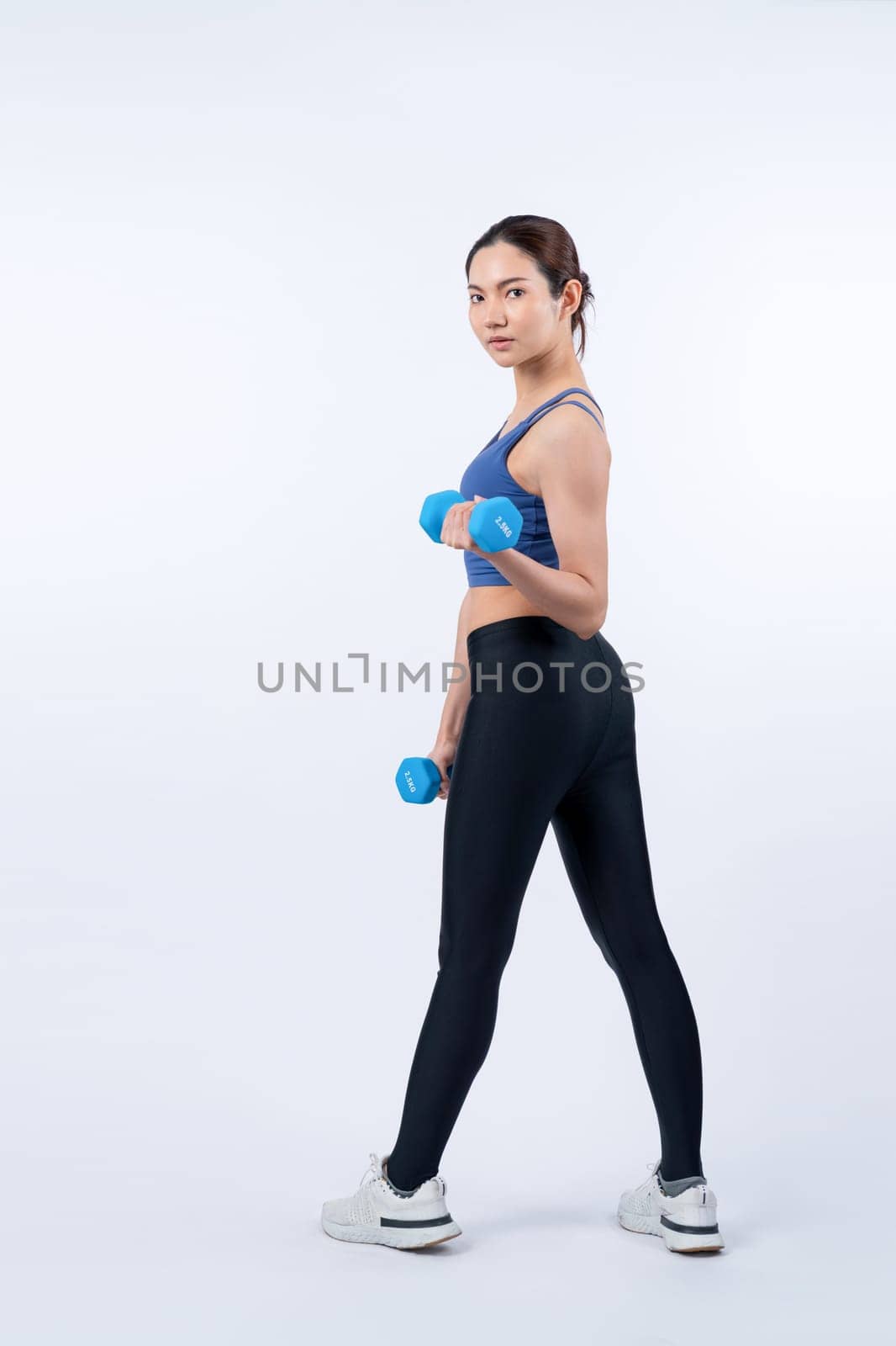 Vigorous energetic woman doing dumbbell weight lifting exercise on isolated background. Young athletic asian woman strength and endurance training session as body workout routine.