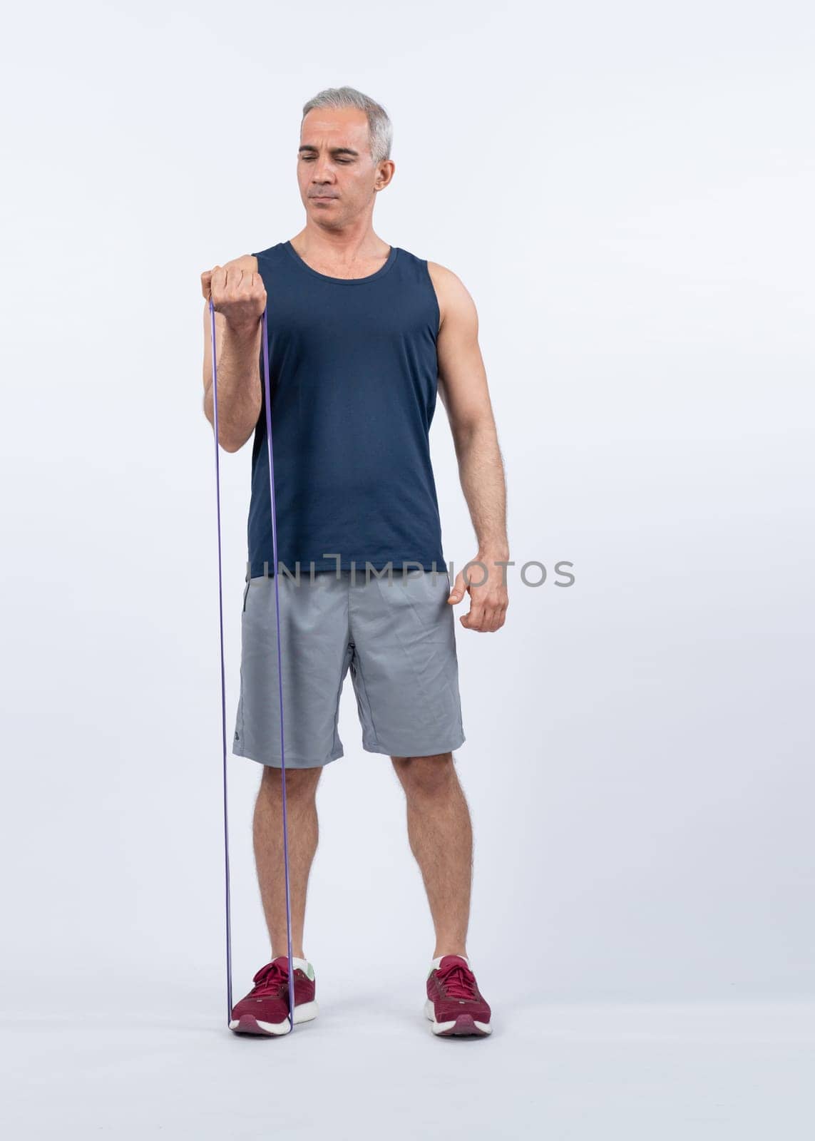 Full body length shot athletic and sporty senior man with fitness resistance band on isolated background. Healthy active physique and body care lifestyle after retirement. Clout