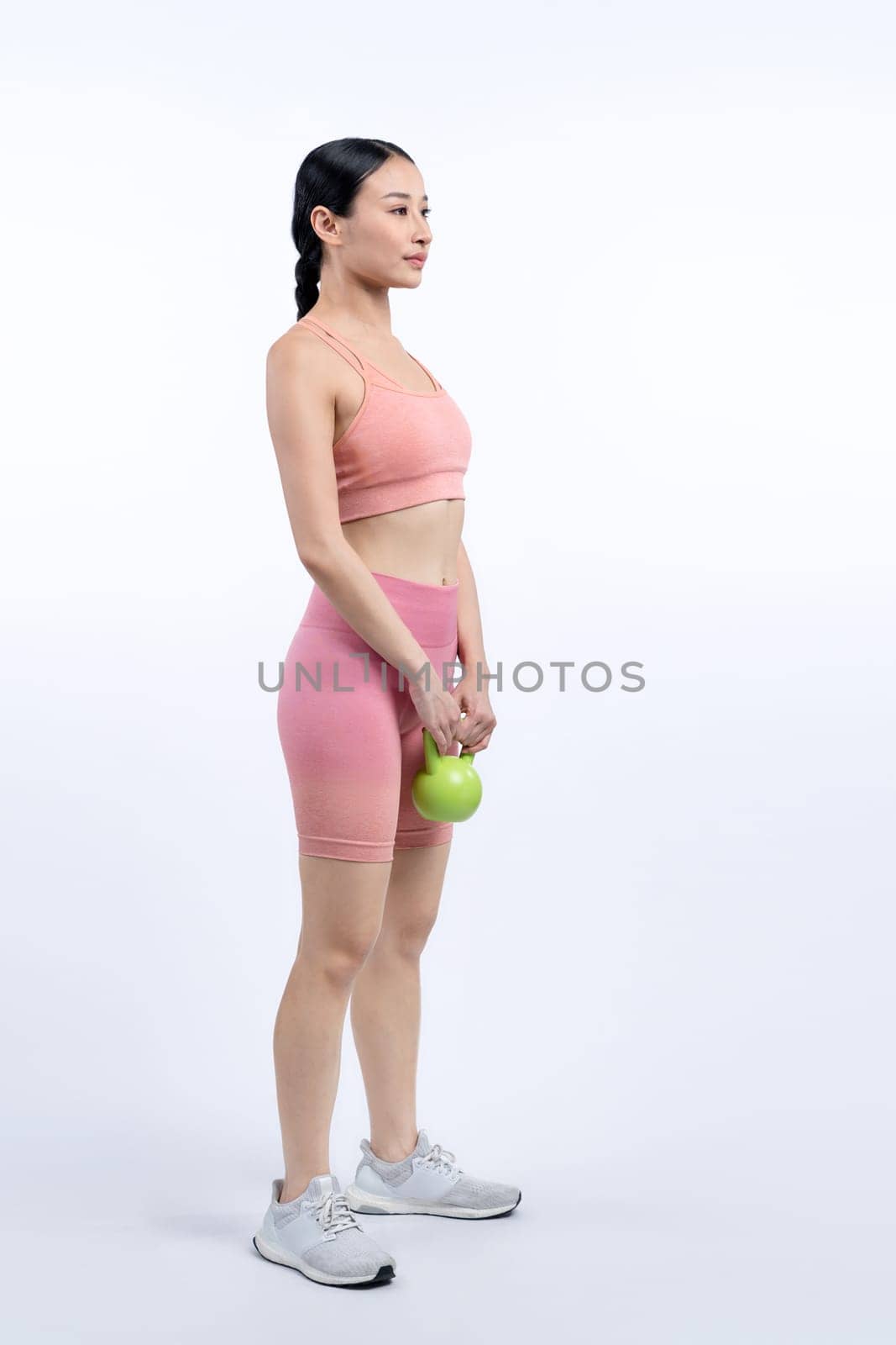 Vigorous energetic woman doing kettlebell weight lifting exercise on isolated background. Young athletic asian woman strength and endurance training session as body workout routine.