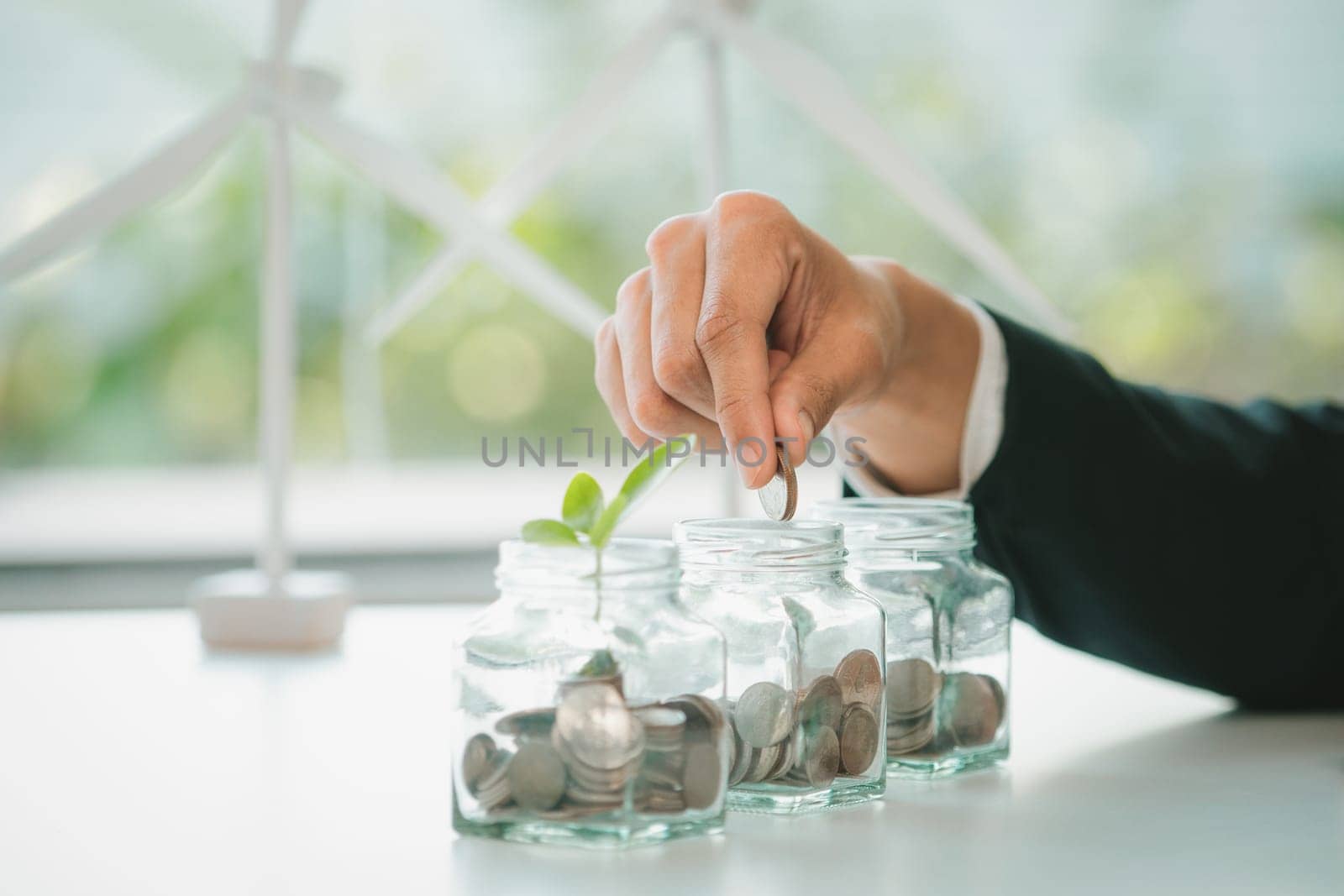 Businessman put coin to money saving glass jar at his office as sustainable money growth investment or eco-subsidize. Green corporate promot and invest in environmental awareness. Gyre