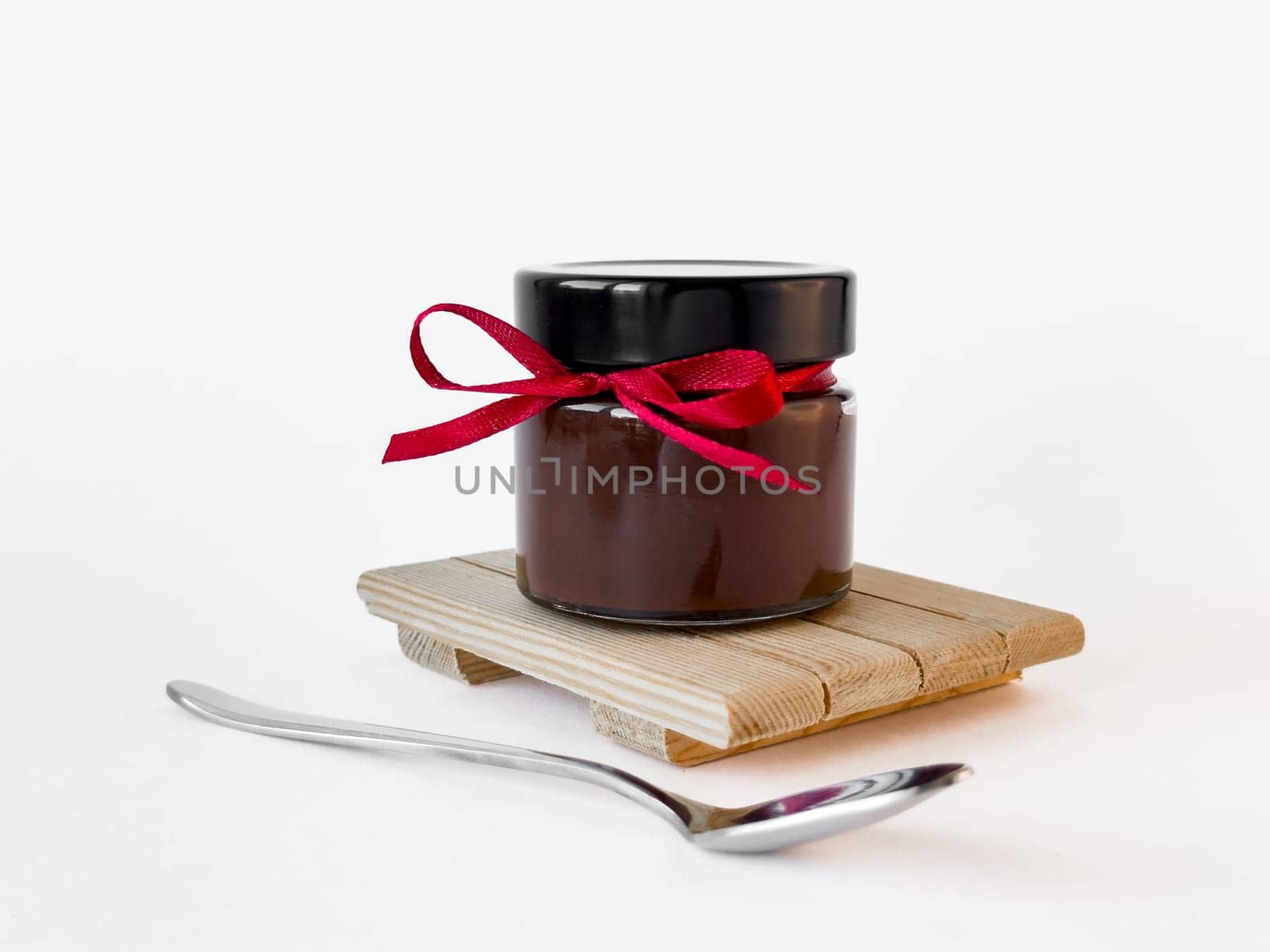 Elegant chocolate jar with red ribbon on wooden stand.