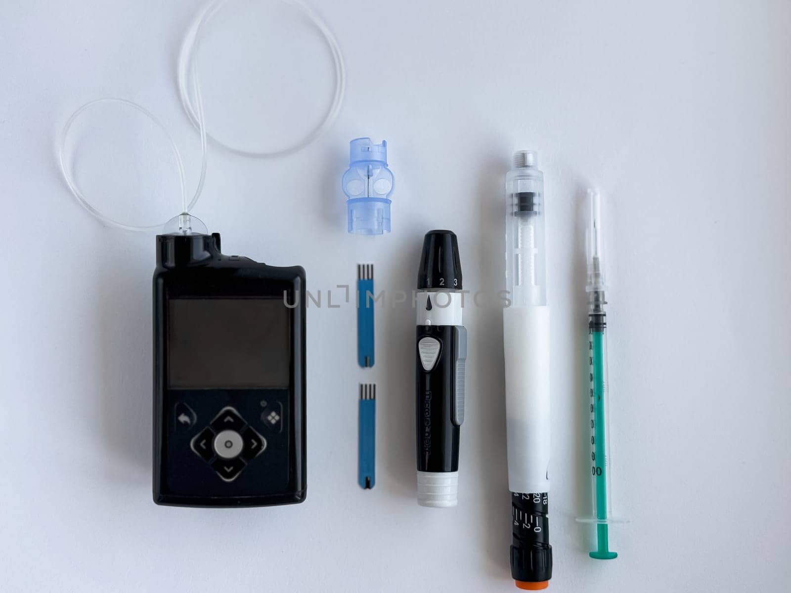 Diabetes management tools, insulin pump, glucometer, and injection supplies on white surface.
